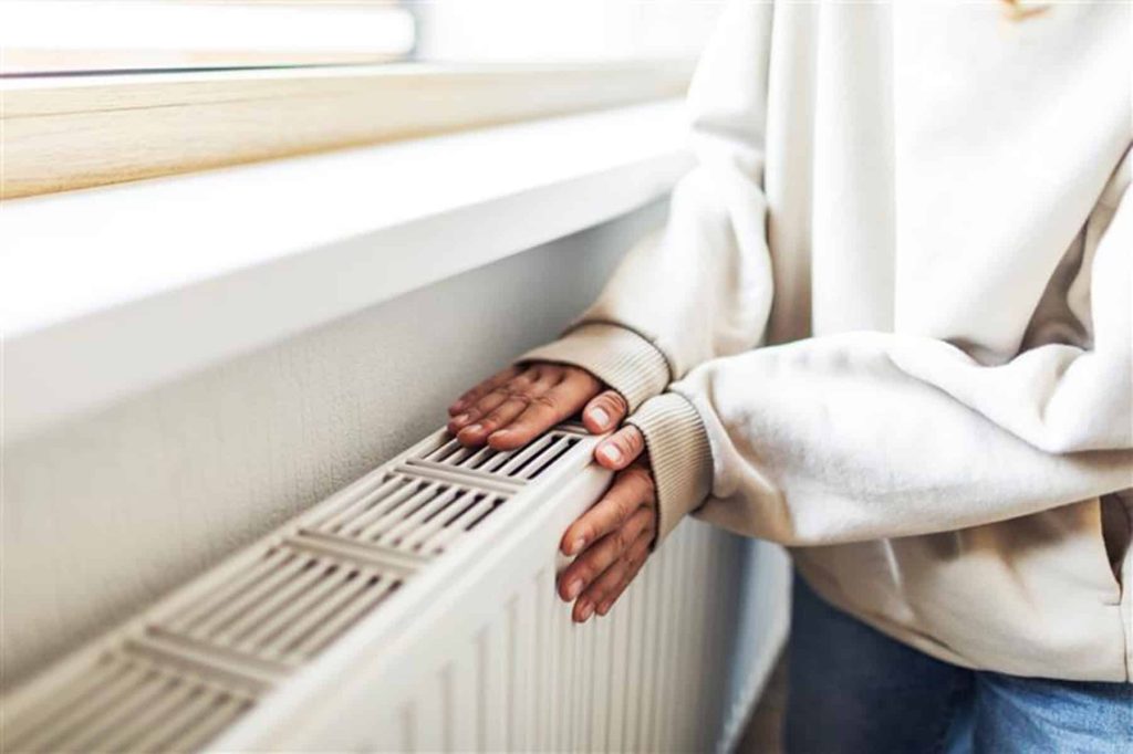 Image shows someone warming their hands on a radiator