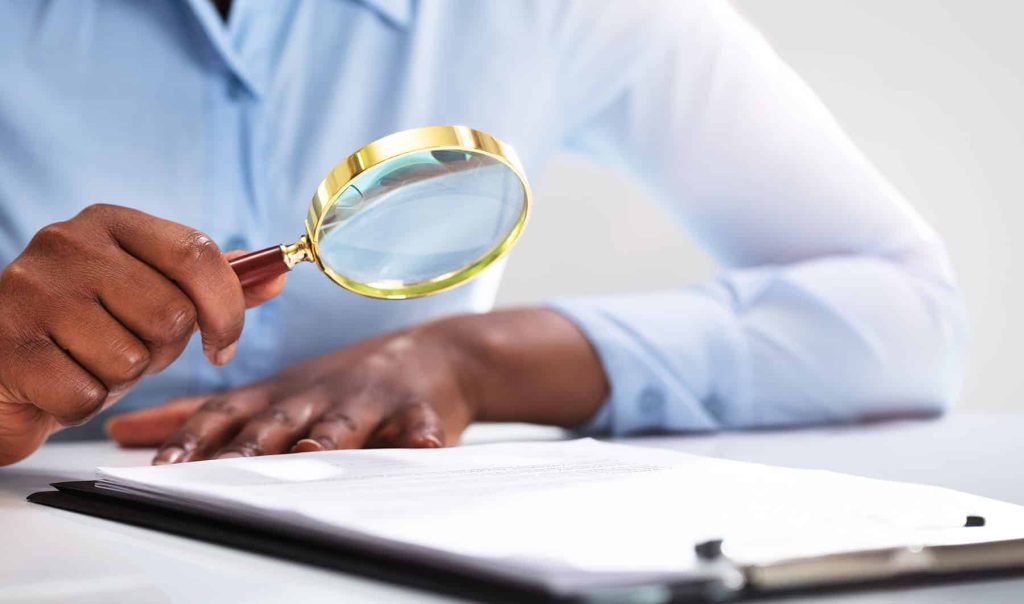 Magnifying glass inspecting a heat pump component for certification standards.