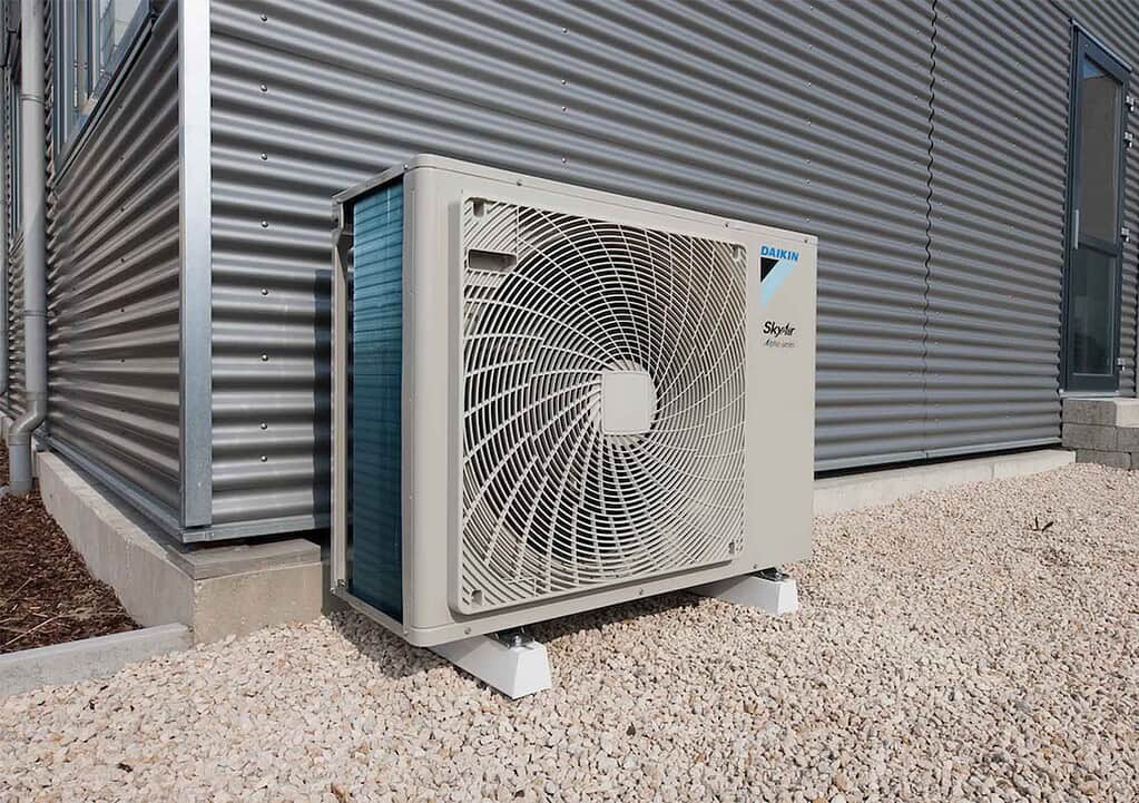 Modern heat pump outdoor unit installed outside a building with metal cladding.