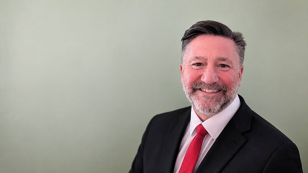A professional man in a suit with a red tie smiling confidently, representing expertise in heat pump.
