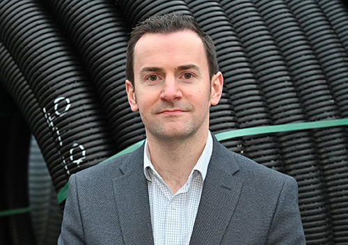 Professional installer standing in front of heat pump pipes, promoting renewable energy solutions.