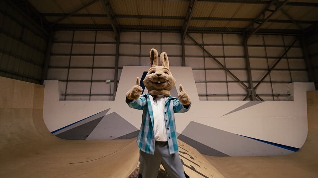 Person in a rabbit mascot costume at skate park with ramps and graffiti.