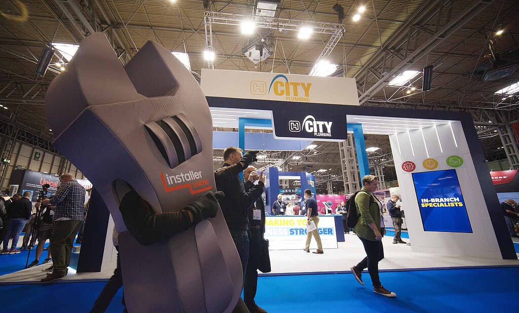 Large wrench mascot at a renewable energy trade show with City Plumbing branding.
