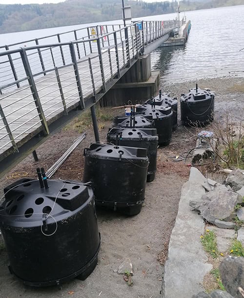 Black floating solar-powered water quality monitoring buoys near a lakeside dock.