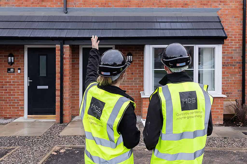 Two MCS inspectors in high-vis jackets inspecting a house exterior.