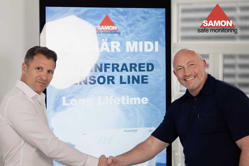 Two men shaking hands in front of a digital display at a heat pump event.