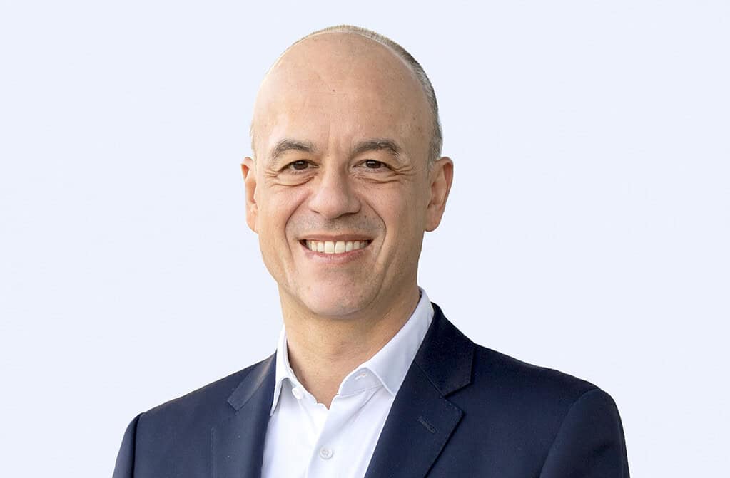 Professional portrait of a smiling man in a suit against a light background.