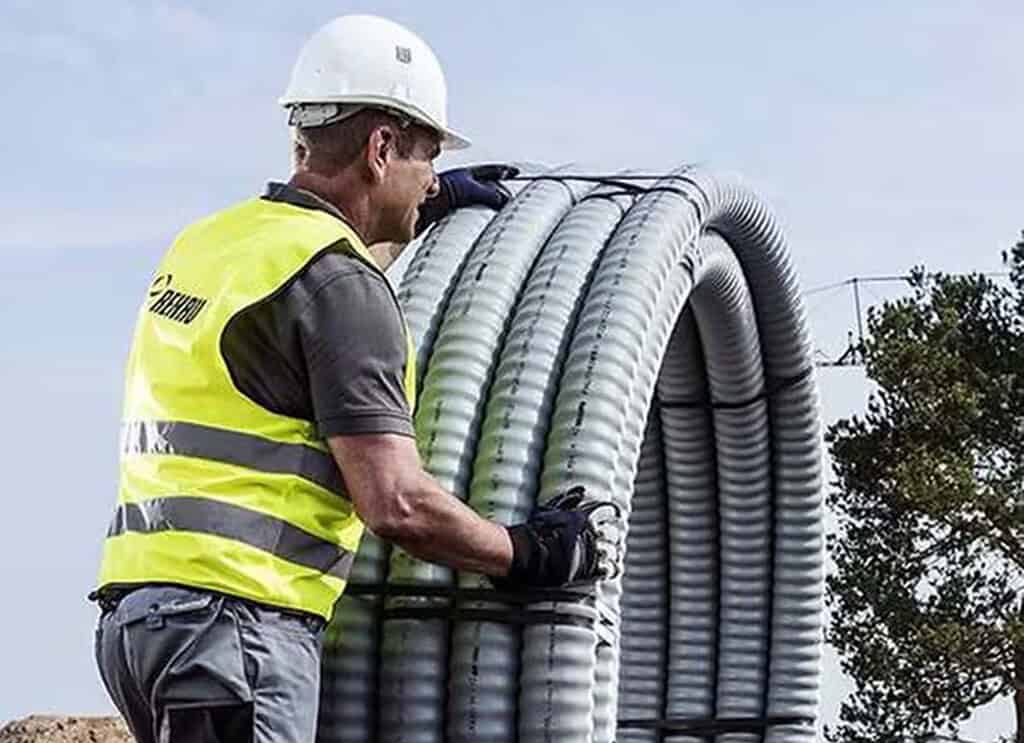 Worker installing insulated district heating pipes outdoors.