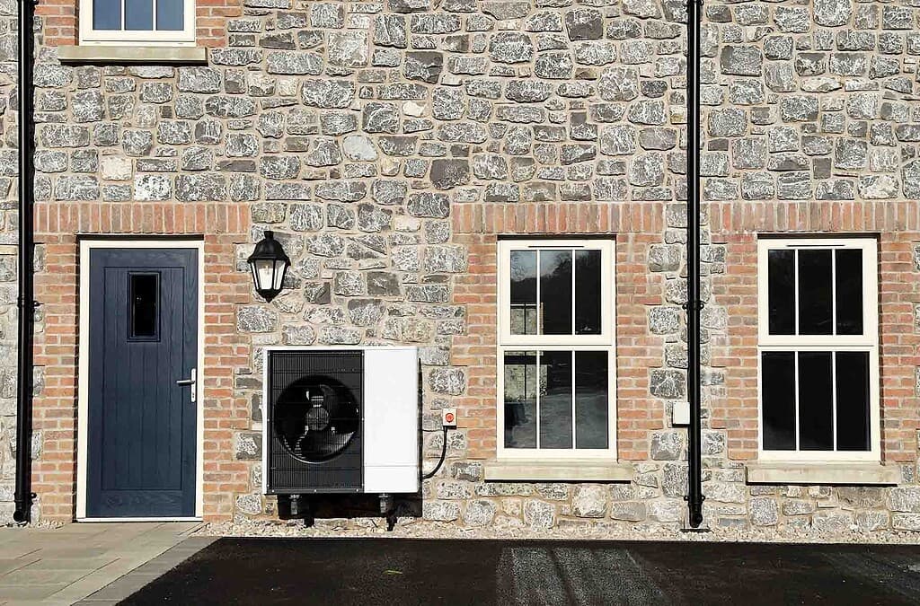 Modern heat pump unit installed outside a stone house with windows and door.