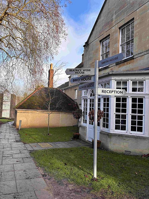Signpost with multiple directions outside a historic building in a village setting.