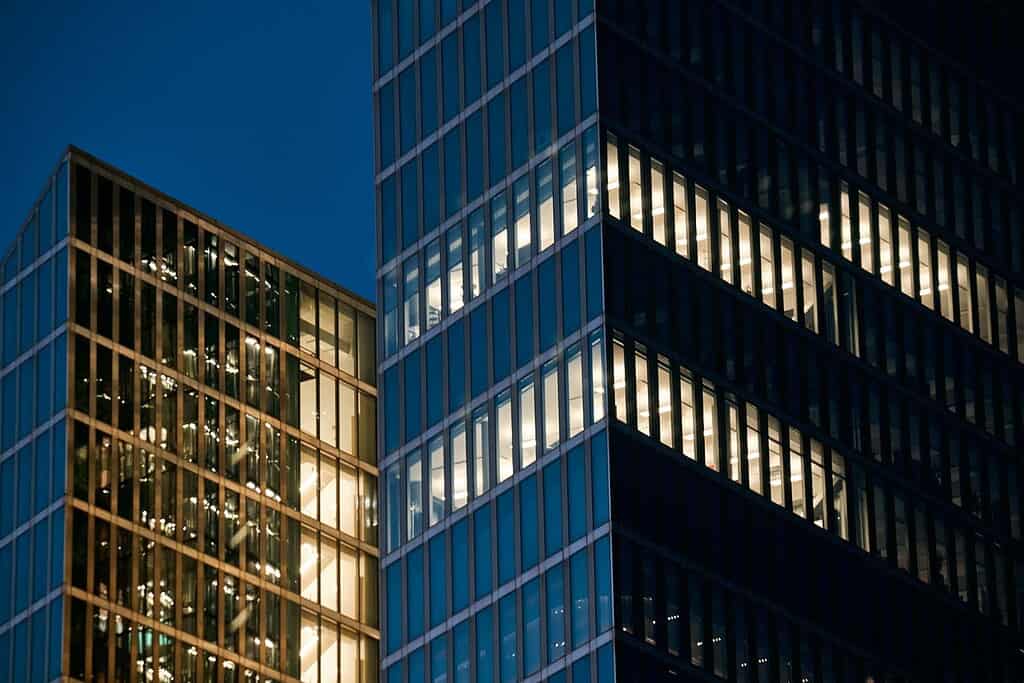 Modern glass office buildings reflecting city lights at night.