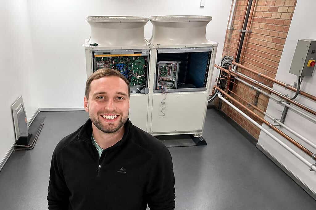 Technician standing in front of heat pump units in a technical room.