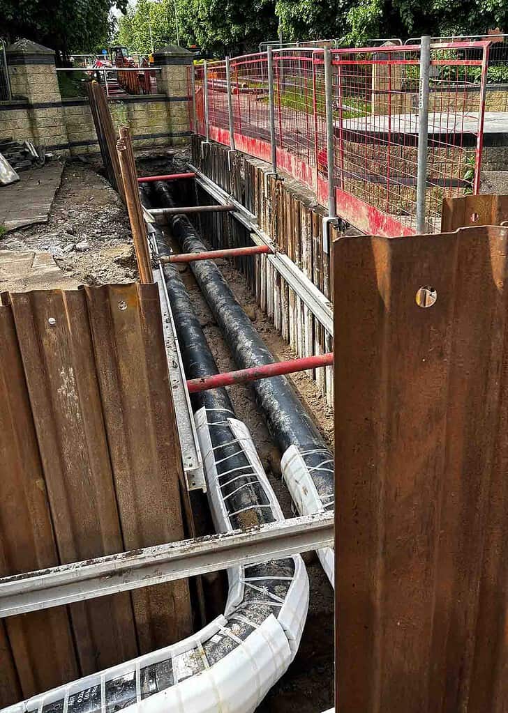 Underground pipes installation for heat network infrastructure with safety barriers.