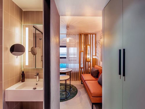 Modern hotel room with a bathroom and seating area, warm lighting, and contemporary decor.