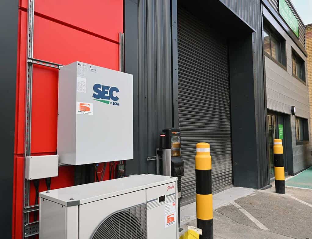 Outdoor SEC heat pump unit installed on building exterior with safety bollards nearby.