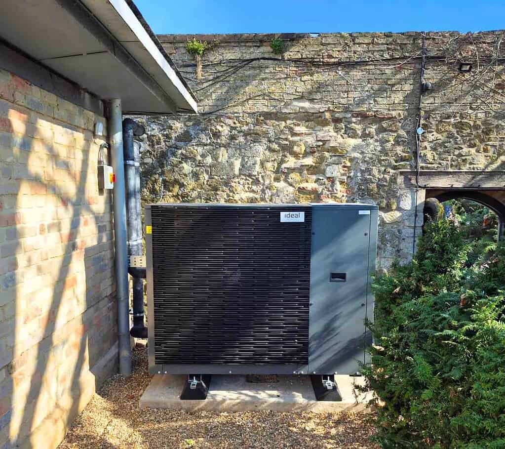 Modern heat pump unit installed outside a historic stone building.