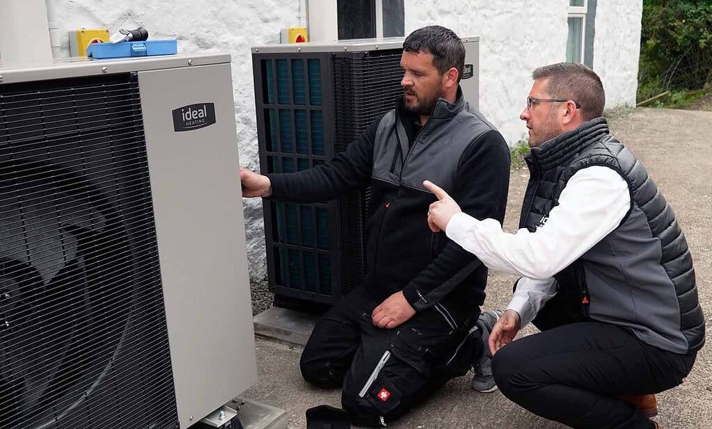 Technicians inspecting a heat pump outside a residential building.