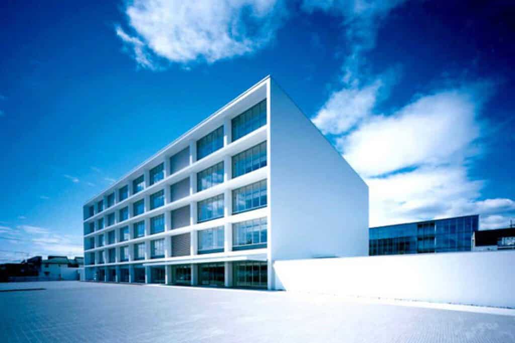 Modern white commercial building with large glass windows under a blue sky.