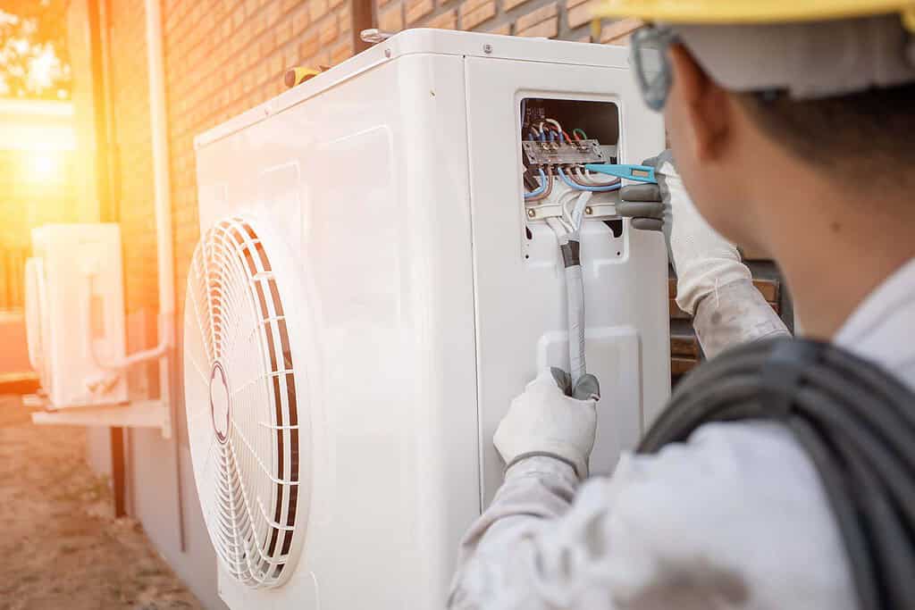 Technician installing or repairing a heat pump outdoor unit in a residential setting.
