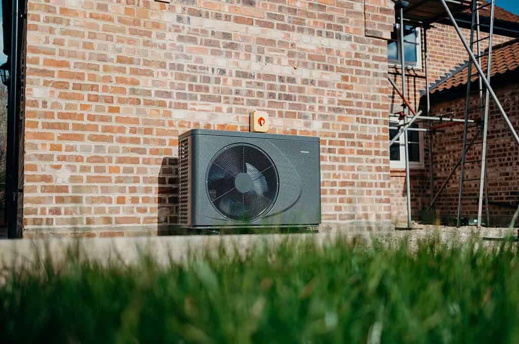 Air source heat pump unit installed on brick wall of a cottage.