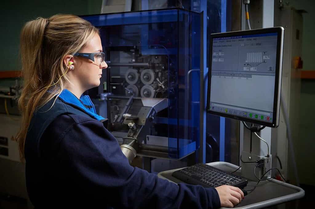 Female technician working with industrial equipment and computer monitor.