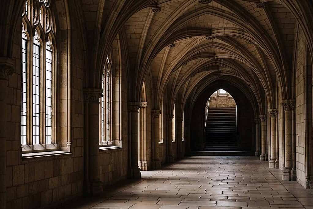Gothic stone corridor with arched windows and vaulted ceiling.
