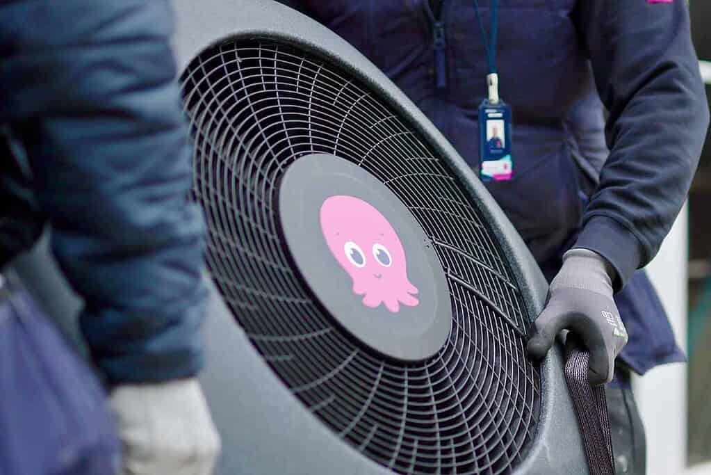 Technicians handling a large heat pump with octopus logo in a professional setting.