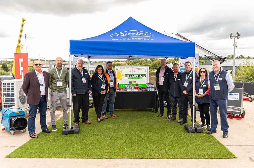 Group of professionals at a heat pump exhibition under a blue canopy.