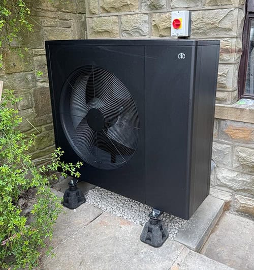 Ground source heat pump unit installed outside a stone building for renewable energy.