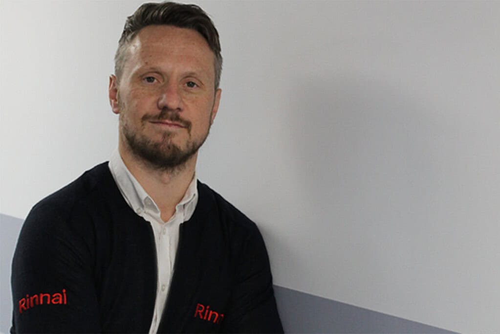 Man in Rinnai branded jacket standing against a plain wall.