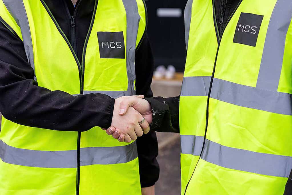 Two installers shaking hands in high-visibility jackets with MCS logo.
