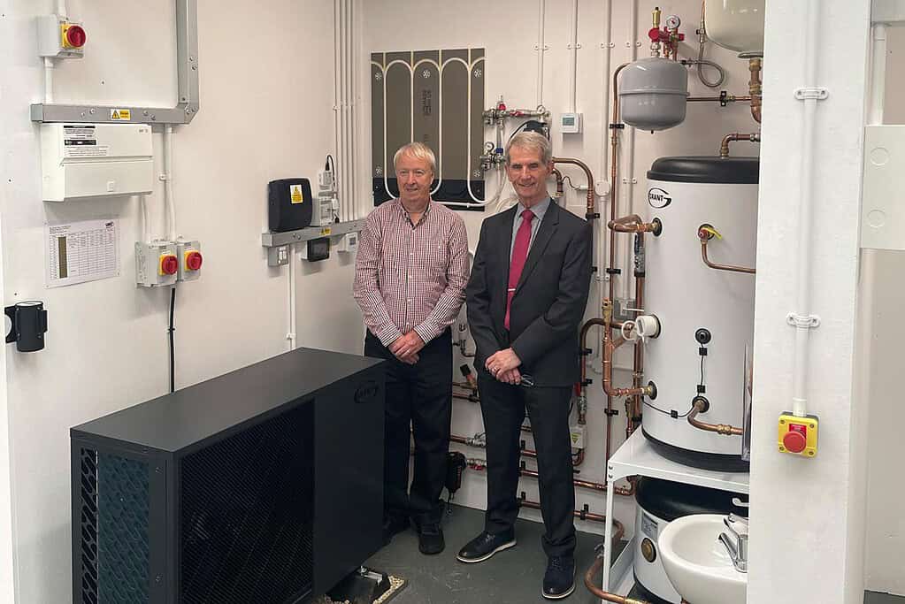 Two men in a technical room with heat pump equipment and control panels.