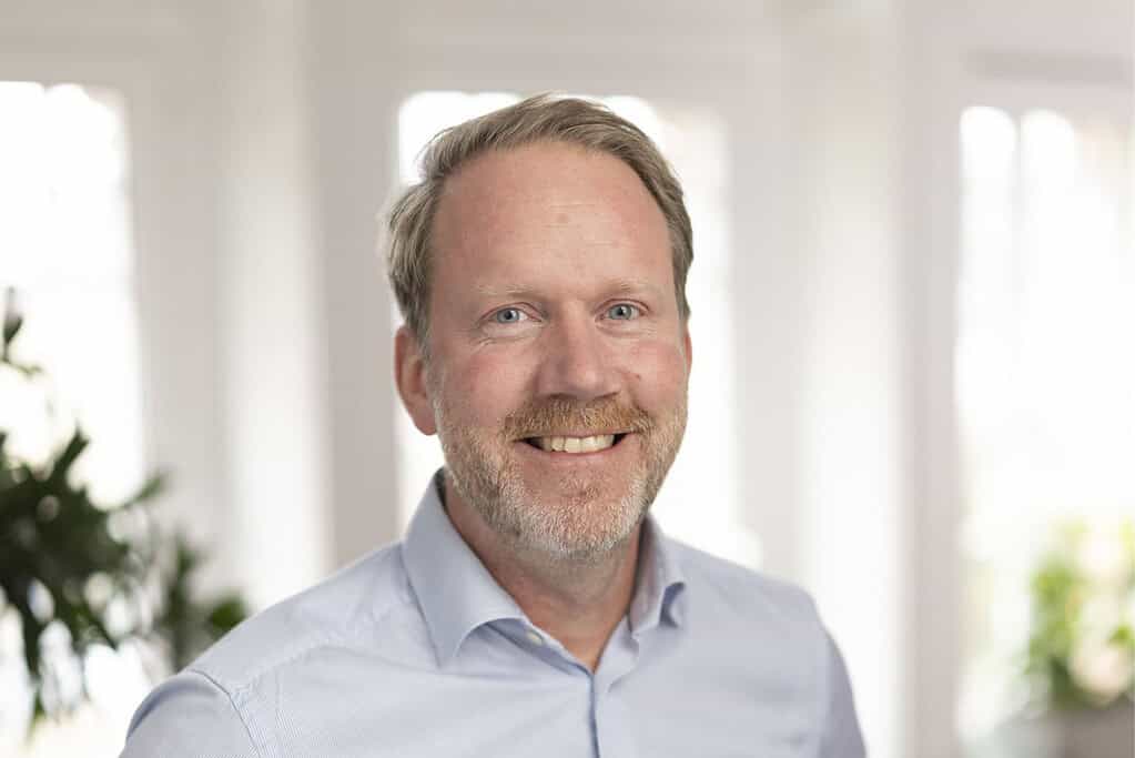 Smiling man in a light blue shirt in a bright office environment.