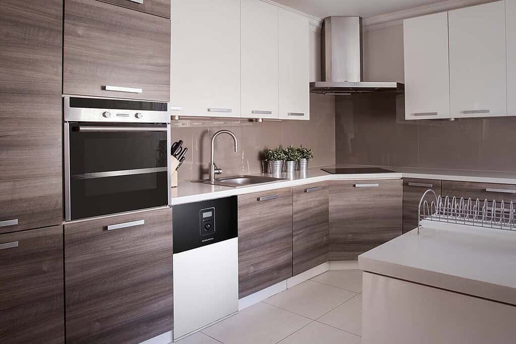 Modern kitchen with built-in oven, sink, and white and wood cabinets.