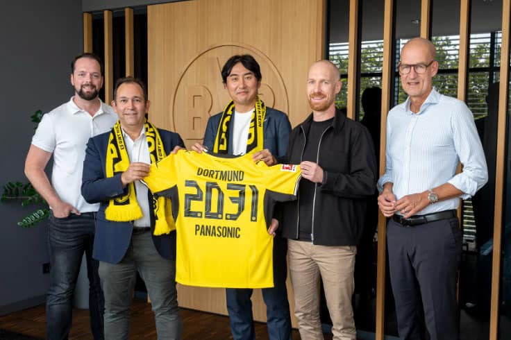 Group of five men holding Dortmund football jersey in office setting.