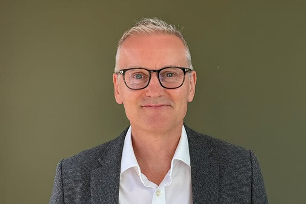 Businessman wearing glasses and a grey blazer against a green background.