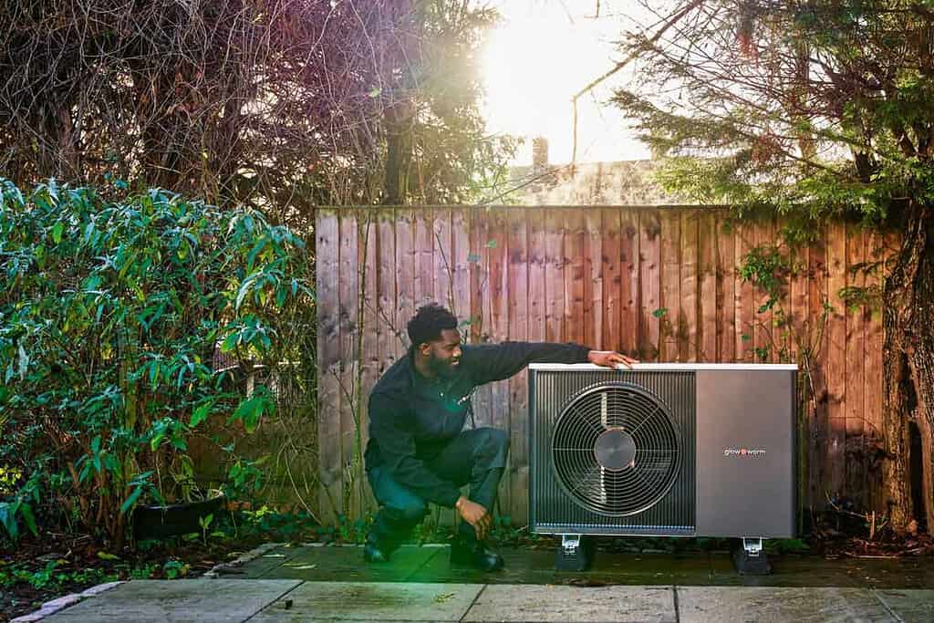 Technician installing or maintaining a heat pump outdoors in a garden setting.